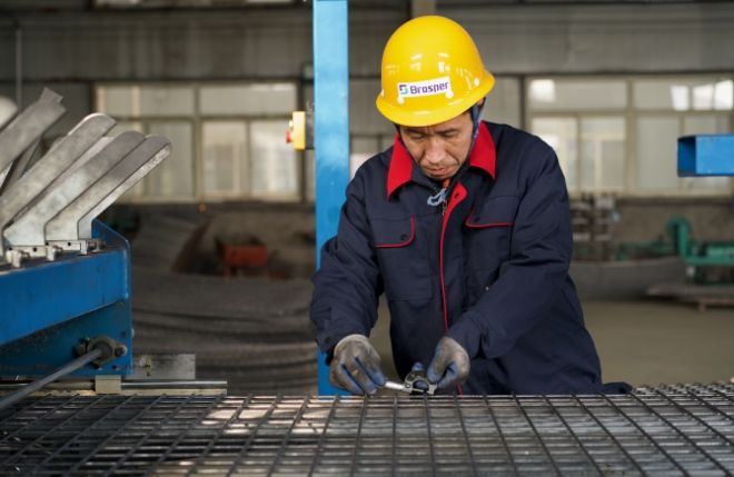 A worker is inspecting the wire diameter of collapsible mesh container panel.