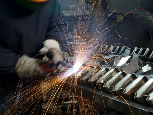 Two workers are welding the feet of wire container panels.