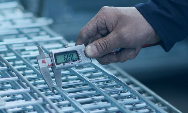 Un trabajador está midiendo el diámetro del alambre del panel del contenedor de alambre.